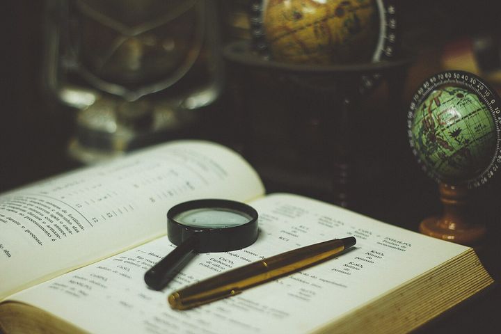 A magnifying glass and pen resting on an open book